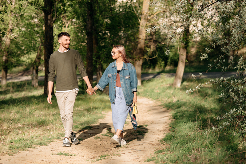 Twee mensen hand in hand wandelen door het bos en glimlachen
