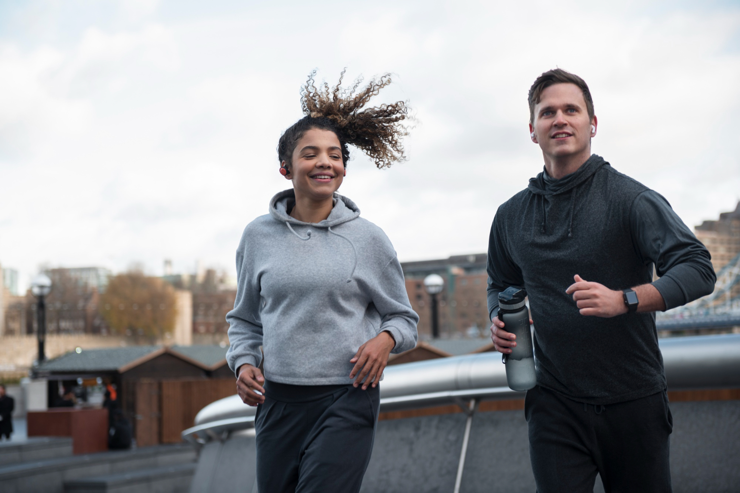 Een man en een vrouw in sportkleding zijn aan het bewegen op een helling. Op de achtergrond zijn gebouwen te zien.