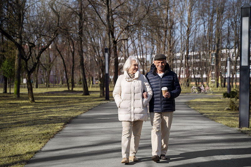 Oud koppeltje met jassen aan loopt in het park en doen aan valpreventie